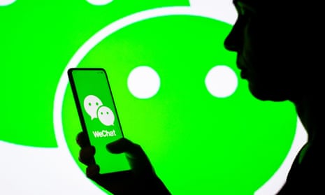 In this photo illustration, a woman's silhouette holds a smartphone with the WeChat logo displayed on the screen and in the background
