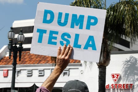 A hand holds a sign saying ‘Dump Tesla’