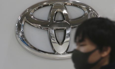 A man wearing a face mask walks by the logo of Toyota Motor Corp. at its showroom in Tokyo. 