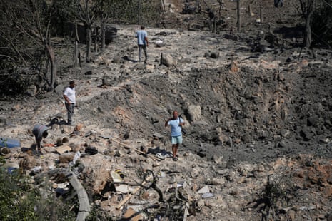People stand near a crater from a bombing.