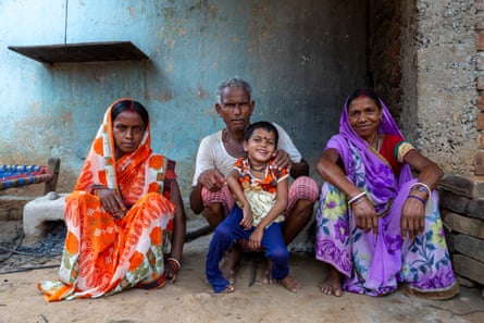 Two women wearing saris and a man with a child on his lap squat on the floor