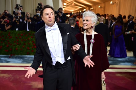 Elon Musk on the red carpet at the 2022 Met Gala wearing white tie and tails, with his mother, Maye, wearing a dark red velvet dress and long strings of pearls