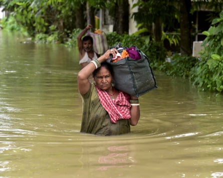 People including a woman up to her waist in water wade through a flood-affected area with their belongings in Sivasagar, Assam, India on 23 July