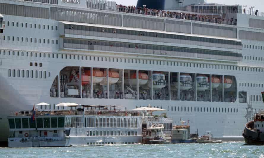 The cruise ship next to the smaller tourist boat in Venice