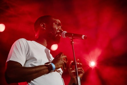 Idehen sings into microphone under red stage lights