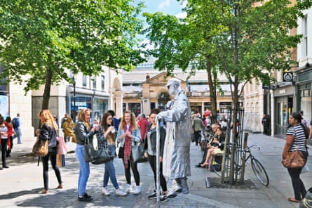 A group of teenage girls look at a man painted in silver and suspended in midair
