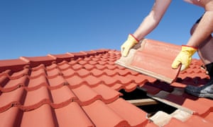 A worker replaces red roof tiles on a house