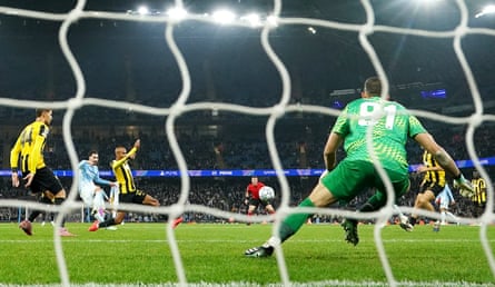 Rayan Cherki shoots past the goalkeeper to score, seen through the goal netting