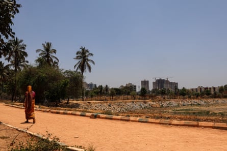A woman wearing a red sari walks along a red dirt path under a cloudless blue sky.