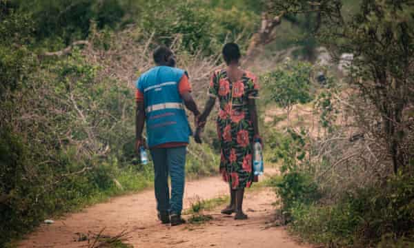 A rescued follower (R) from the forest is supported by a volunteer