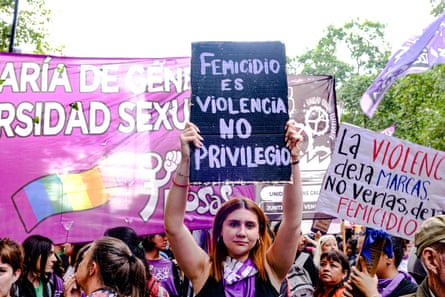 Women march holding placards with slogans denouncing violence against women. Many wear purple.