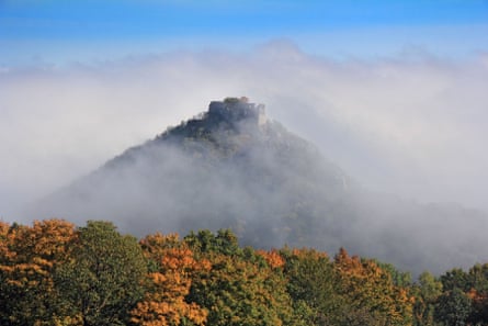 The mist-shrouded ruins of a castle on top of a hill.
