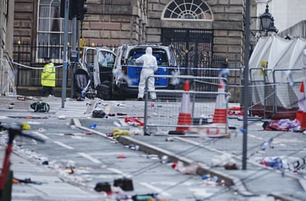 Forensic officers standing beside their vehicle amid a scene of abandoned belongings and litter on the street