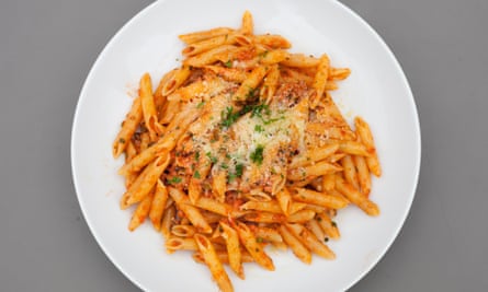 A large round white plate of penne with sausage sauce.