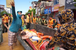 Soldiers and beneficiaries stand in knee-deep water around a boat carrying supplies on an urban street