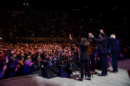 three people stand with their hands held high toward a stadium full of people
