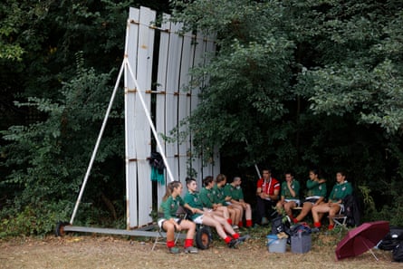 Members of the Basque Country women’s U23 500kg team shelter from the rain next to a cricket sight-screen.