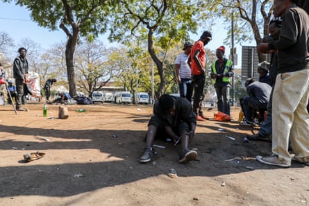 A man injects himself in the leg while sitting on the ground by a road in a city