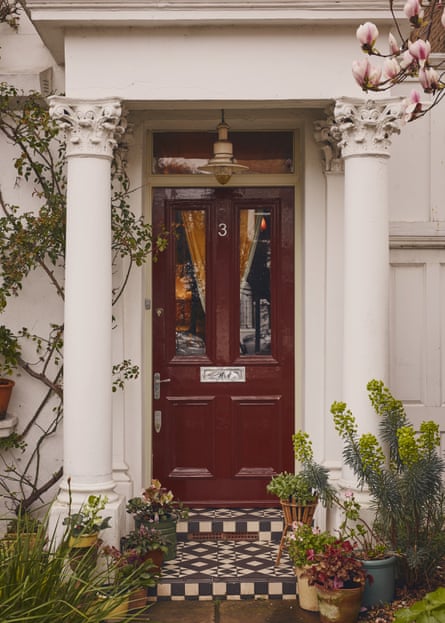 A dark red front door with potted plants on a black and white tiled path leading to it