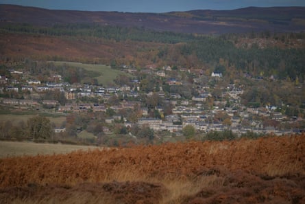 View from the estate through reddish bracken to a small town with stone buildings on the opposite hillside with more hills behind it.