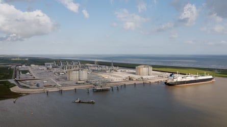 An LNG facility on a body of water with a ship in the foreground.