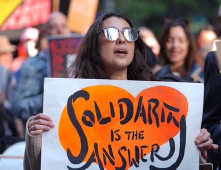 Woman with sunglasses holds orange and white sign that says Solidarity Is the Answer.