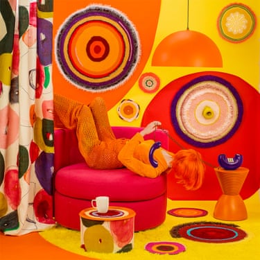 a woman holding a phone while sitting on chair in a colorful, 1970s-esque room