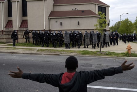 A young man stands with his arms outstretched across the street from police in riot gear
