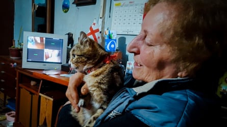 A woman holds a cat while a screen in the background shows four CCTV views.