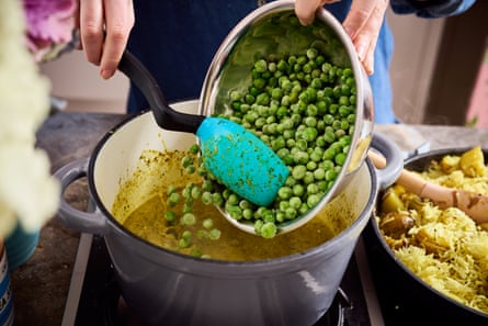 Peas being spooned into a dal base in a pot