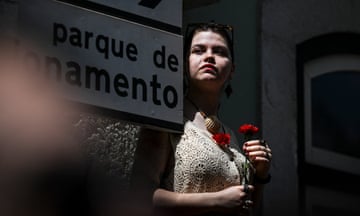 A woman holds a red carnation during a military parade.