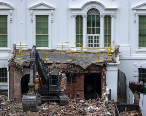 excavator on top of rubble as part of white building is demolished