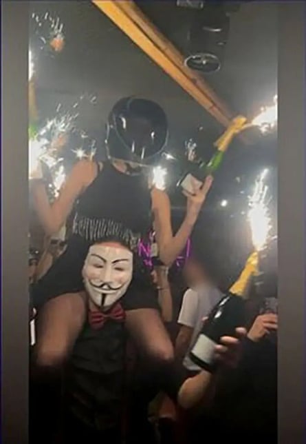 Woman in helmet holding a sparkler and sitting on the shoulders of someone wearing a mask. This image may have been subjected to some digital enhancement