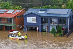 Rescue boat approaches woman standing in flood water outside a house