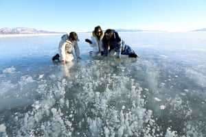 Xinjiang, China: women observe bubbles frozen under the surface of Sayram lake in Bortala