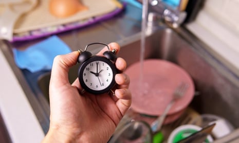 A hand holding a clock over a sink of dirty dishes.