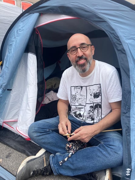 Guillermo Esteve sitting crosslegged in the entrance of his tent, knitting