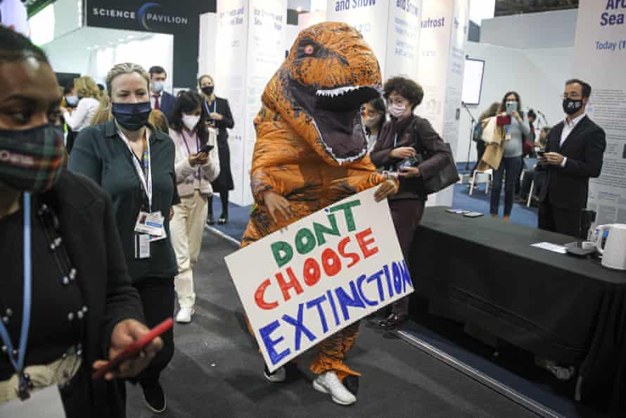 An activist dressed as a dinosaur walks though the pavilion section of Cop26.