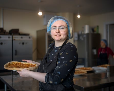A young woman in an apron and hairnet holding a pizza