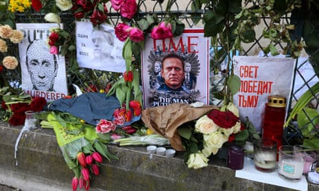 Flowers and candles on a stone ledge, along with a cover of Time magazine featuring an image of Alexei Nalvany. An image of Putin with the word "murderer" is also shown.