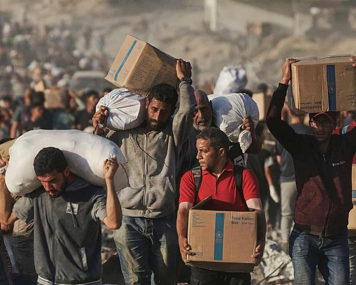 A long line of people carrying cardboard boxes and sacks