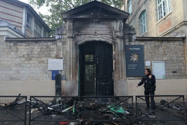 A police officer stands next to the burned entrance of Roger Verlomme secondary school following a blockade by protesting students in Paris