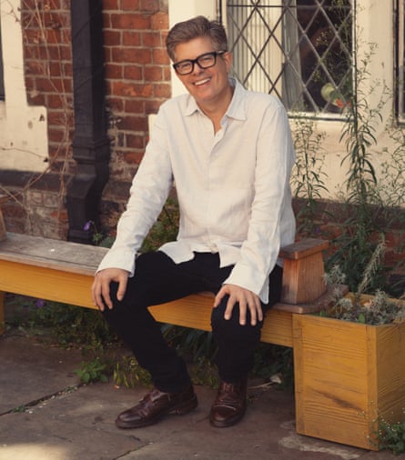 Robert Peckham sitting on a bench outside, plants around him and a latticed window in a brick wall behind him