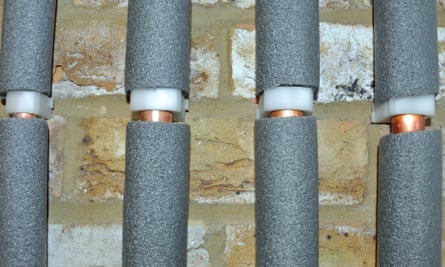 Four water pipes in grey foam insulation against a brick wall.
