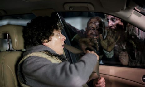 A screenshot from Zombieland. A young man sits in the front driver seat of a car, while zombies look in through the window.
