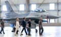Zelenskiy, Rutte, Ollongren and three air force personnel walk in front of an F-16 fighter jet in an aircraft hangar.