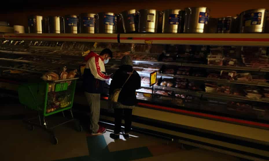 Customers use the light from a cellphone to look in the meat section of a grocery store in Dallas.