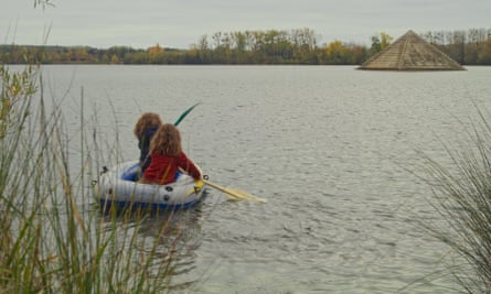 Two girls in an inflatable dinghy paddle towards a pyramid in the middle of the lake