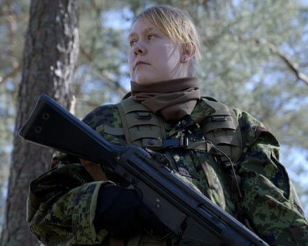 A blonde woman in military fatigues looks in the distance