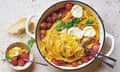 Topview of a pot of angel hair pasta tinged golden with saffron, and topped with cherry tomatoes, burrata and basil.